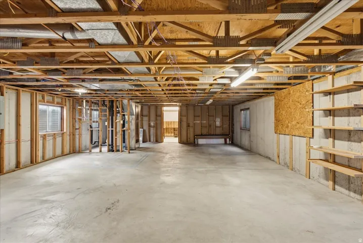 Unfinished basement featuring exposed wood joists, concrete flooring, and built-in shelving