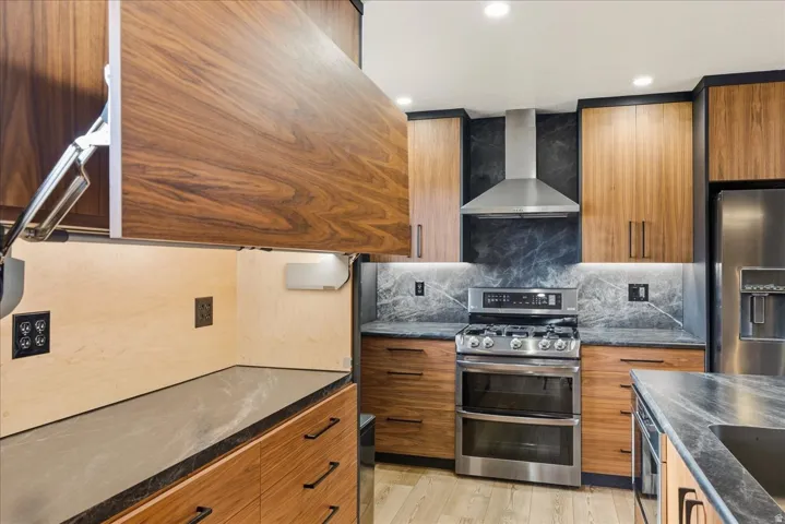 Wood-finish cabinetry, stone slab countertops, stainless steel appliances, under-cabinet lighting, and recessed ceiling lighting