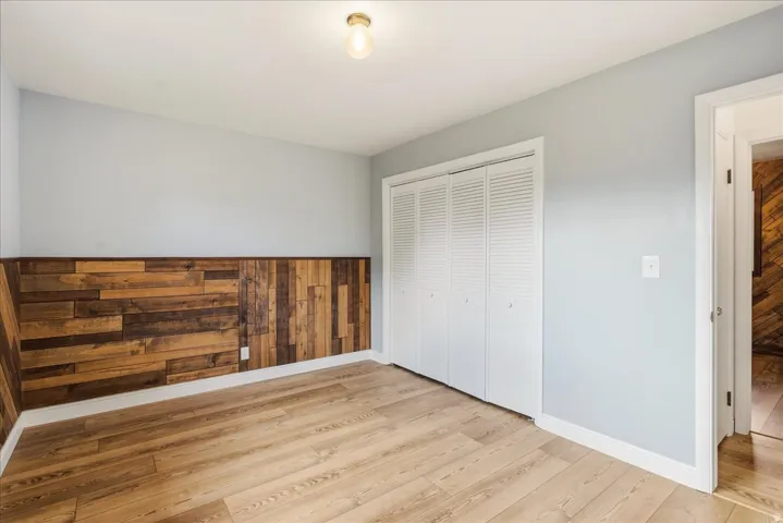 Wood-finish flooring, wood plank accent wall, neutral wall paint, louvered bi-fold closet doors, and recessed lighting