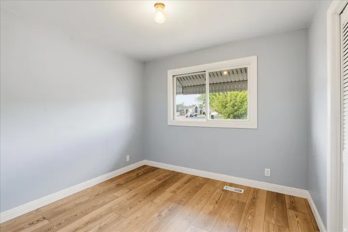 Wood-finish flooring, light blue wall paint, white trim, sliding window, and a built-in closet with louvered doors