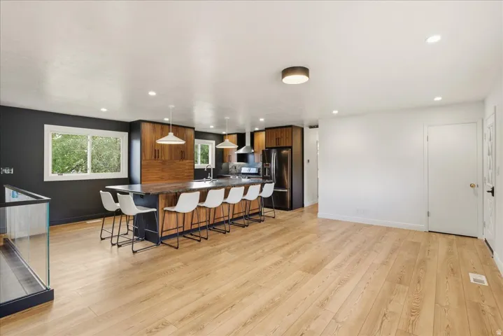 Open-concept living space with wood-finish flooring, a kitchen island with seating, recessed lighting, and a modern kitchen with integrated appliances