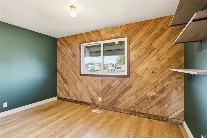 Diagonal wood-panel accent wall, wood-finish flooring, built-in shelving, painted walls, and a single window