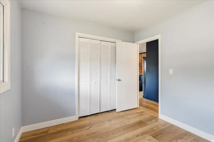 Wood-finish flooring, light blue wall paint, white trim, window with white casing, and louvered bi-fold closet doors