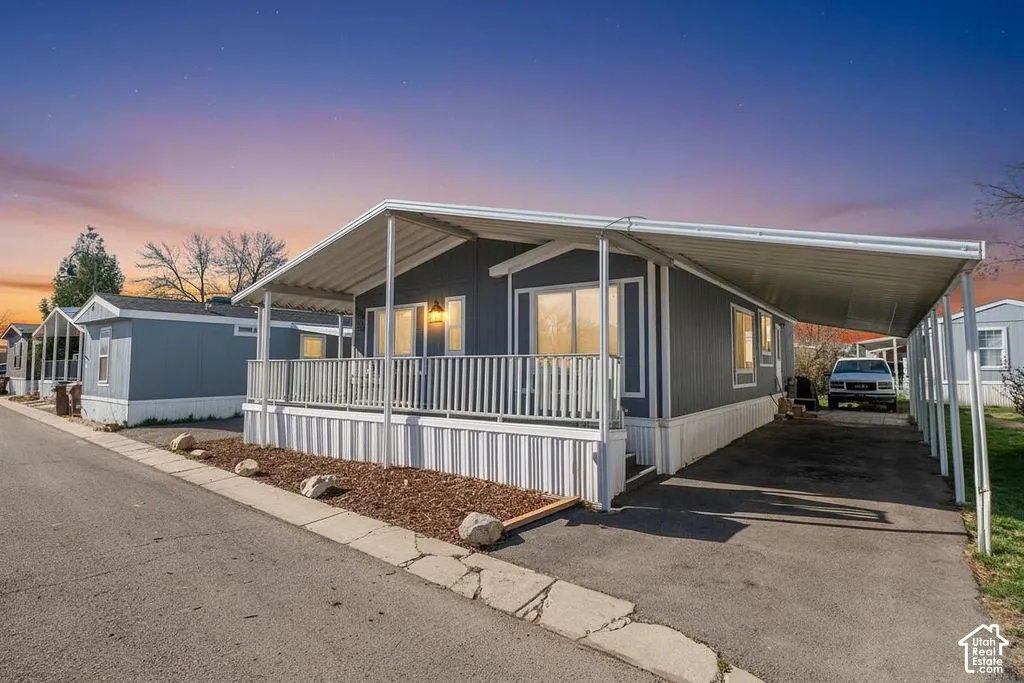 Exterior featuring gray siding, a covered porch with white railings, a white carport, and a landscaped rock and mulch bed
