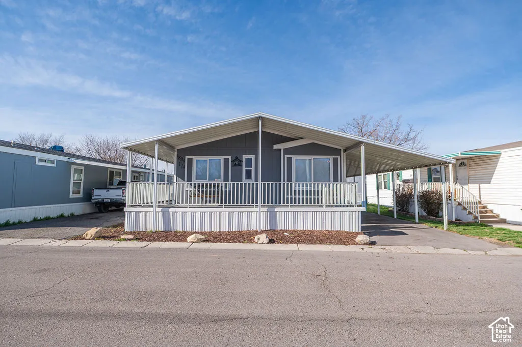 Covered carport parking, covered entry porch with white railing, gray exterior siding, and white window trim