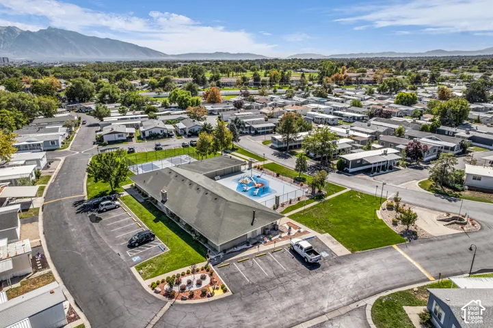 Community grounds featuring a large building with a dark roof, a fenced swimming pool, a separate fenced court, and paved parking areas