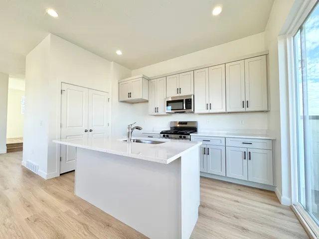 Modern kitchen featuring white shaker-style cabinetry with brushed nickel hardware, a large waterfall-edge island with seating, quartz countertops, stainless steel appliances including a gas cooktop and built-in microwave, and abundant natural light from