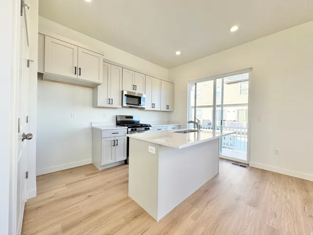 Modern kitchen featuring light cabinetry, stainless steel appliances, a center island with sink, quartz countertops, and light wood-finish flooring
