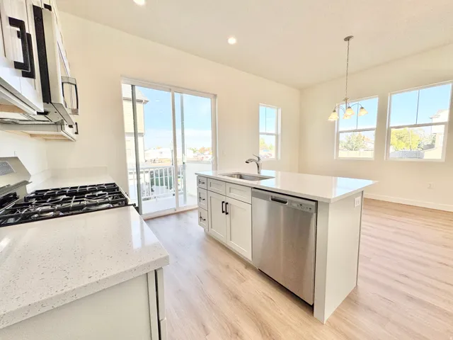 Modern kitchen featuring white cabinetry, light-toned wood-finish flooring, a kitchen island with an integrated sink, white countertops, and stainless steel appliances
