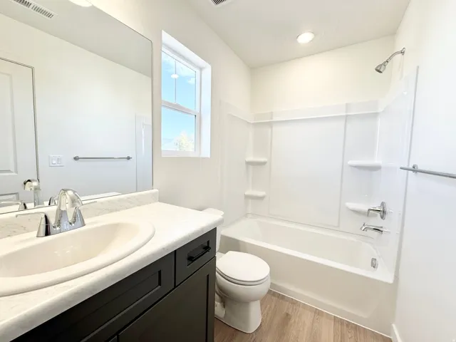Bathroom featuring a dark wood-finish vanity, integrated sink, chrome fixtures, and a combined tub and shower unit