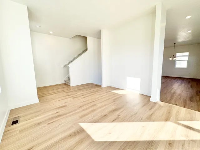 Light wood-finish flooring throughout, recessed ceiling lighting, and a staircase with a white railing