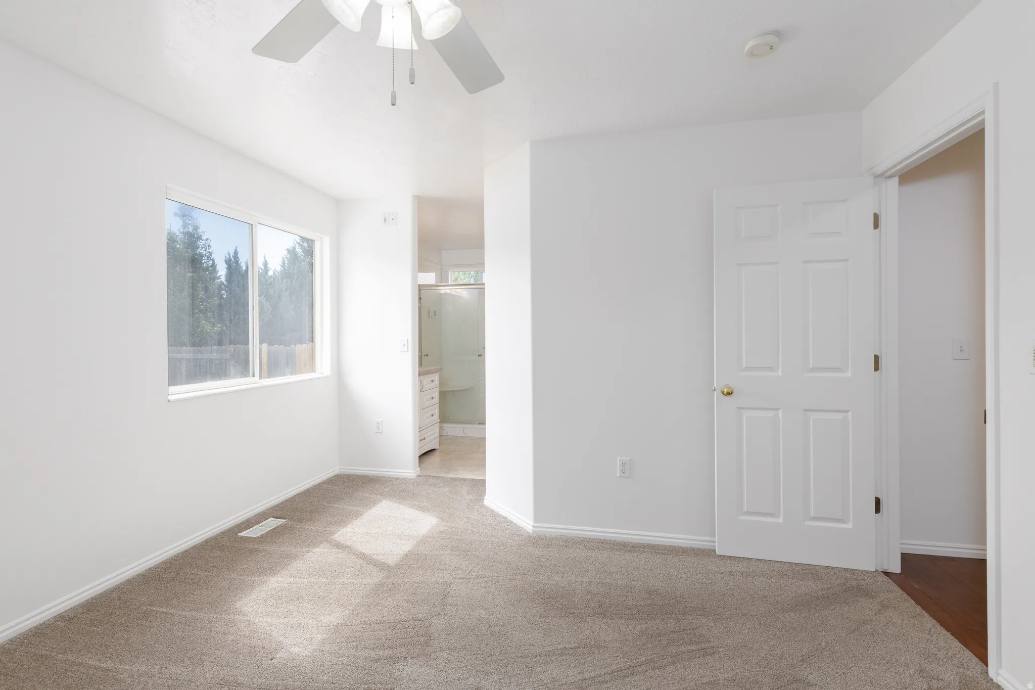 Carpeted flooring, white walls, ceiling fan, large window, and panel door