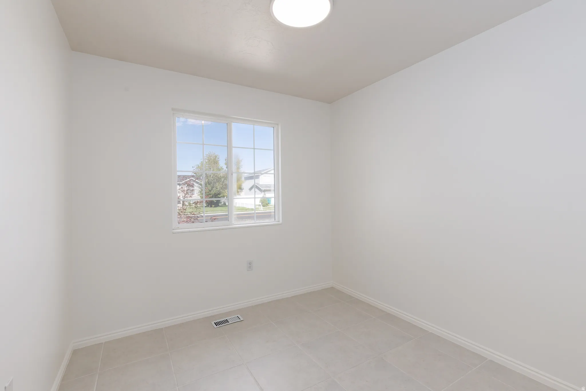Large window with grid pattern, light-colored tile flooring, and a flush-mount ceiling light