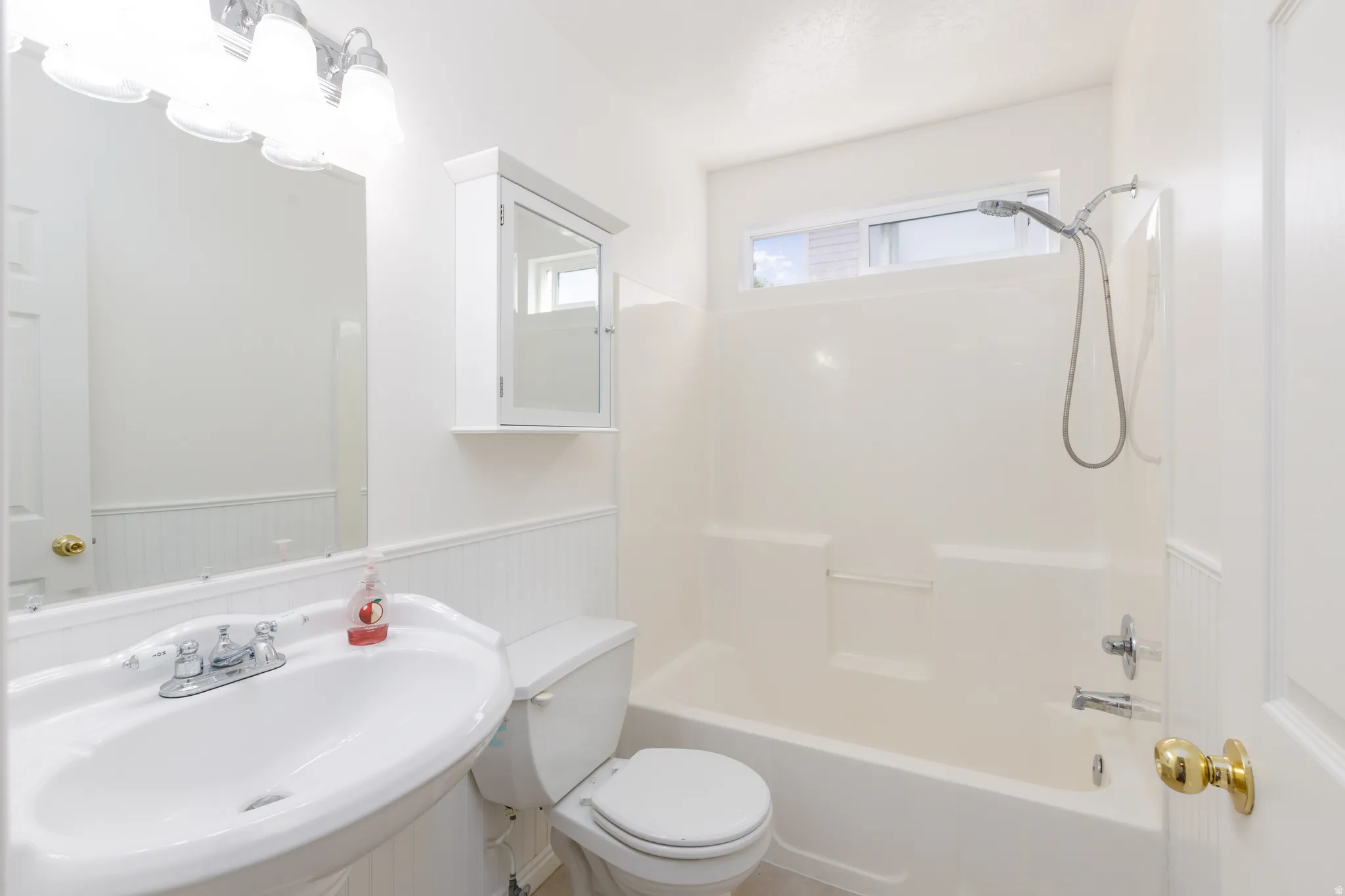 White pedestal sink with chrome faucet, wall-mounted mirror, and overhead vanity lighting
