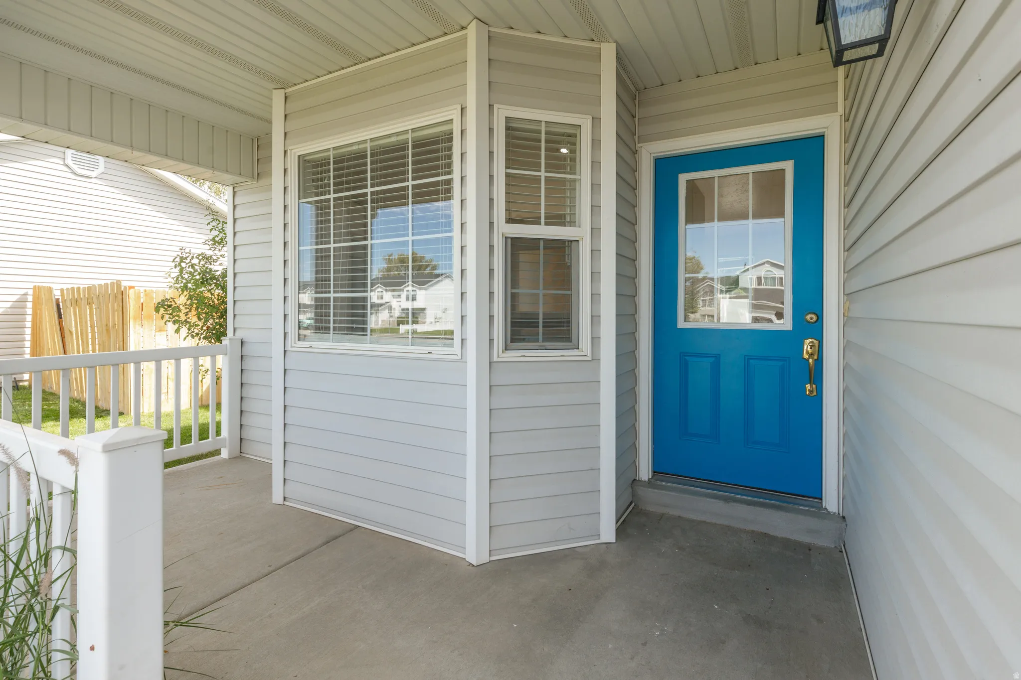Covered porch with concrete flooring, white railing, bay window, and a vibrant blue entry door with glass paneling