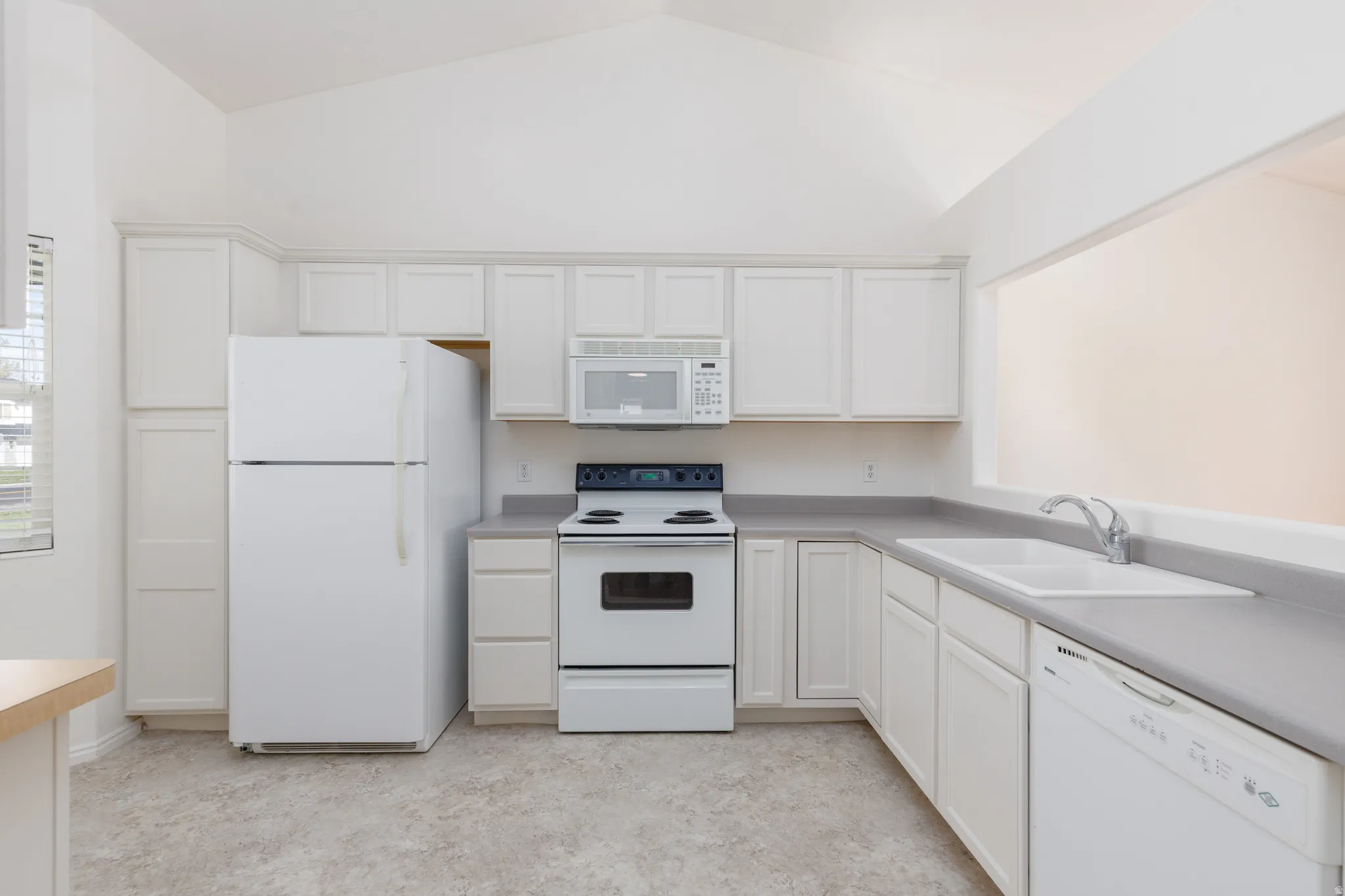 Kitchen featuring vaulted ceilings, white cabinetry, a built-in microwave, a double basin sink, and a white dishwasher