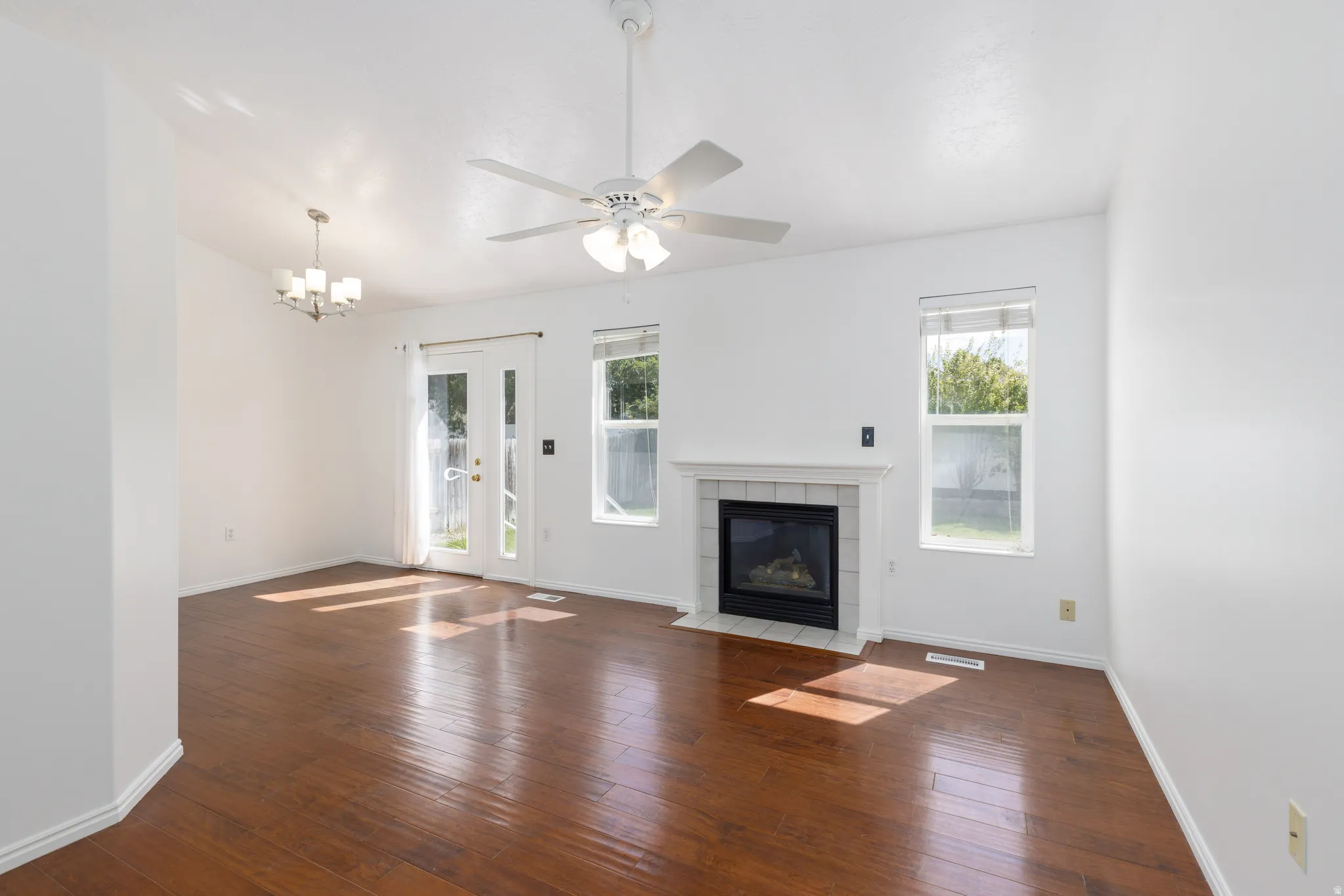 Wood-finish flooring throughout, featuring a white mantle fireplace with tile surround, a ceiling fan, and a built-in chandelier