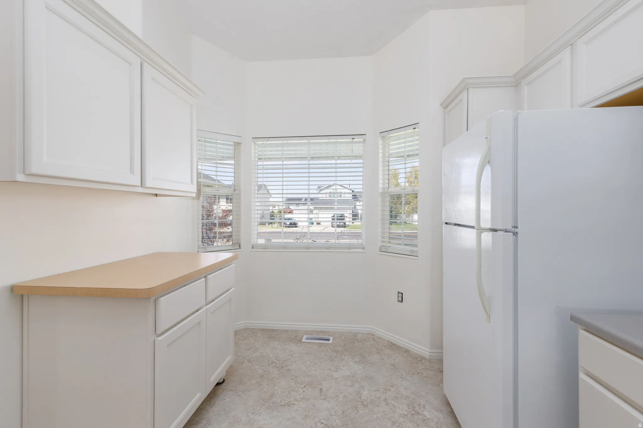 White cabinetry, light-toned countertops, and three windows with blinds