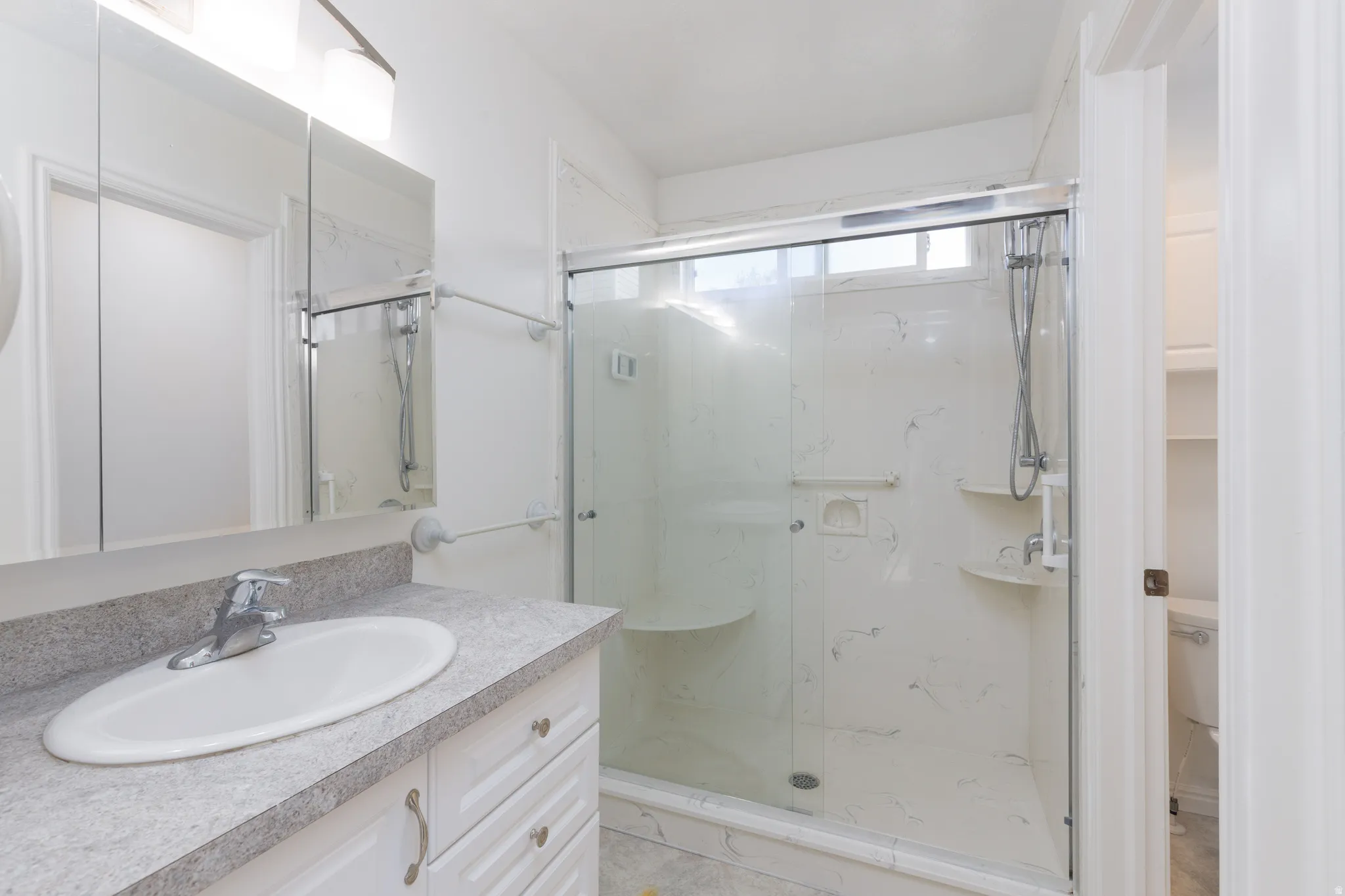 White vanity with an integrated sink and chrome faucet, full-width mirrored medicine cabinet, and a walk-in shower with a glass enclosure