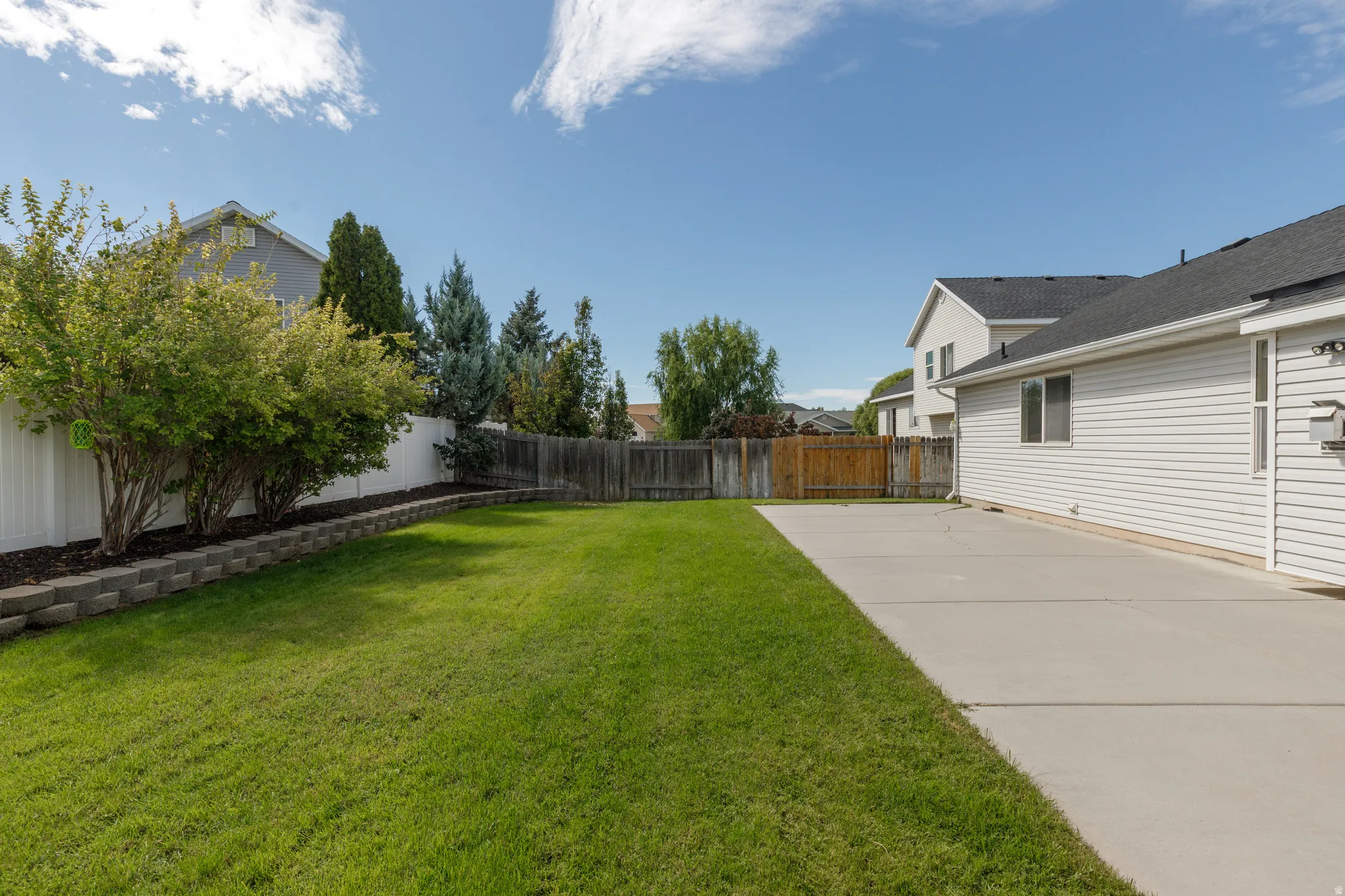 Expansive lawn area with a concrete patio, retaining wall, and mature landscaping
