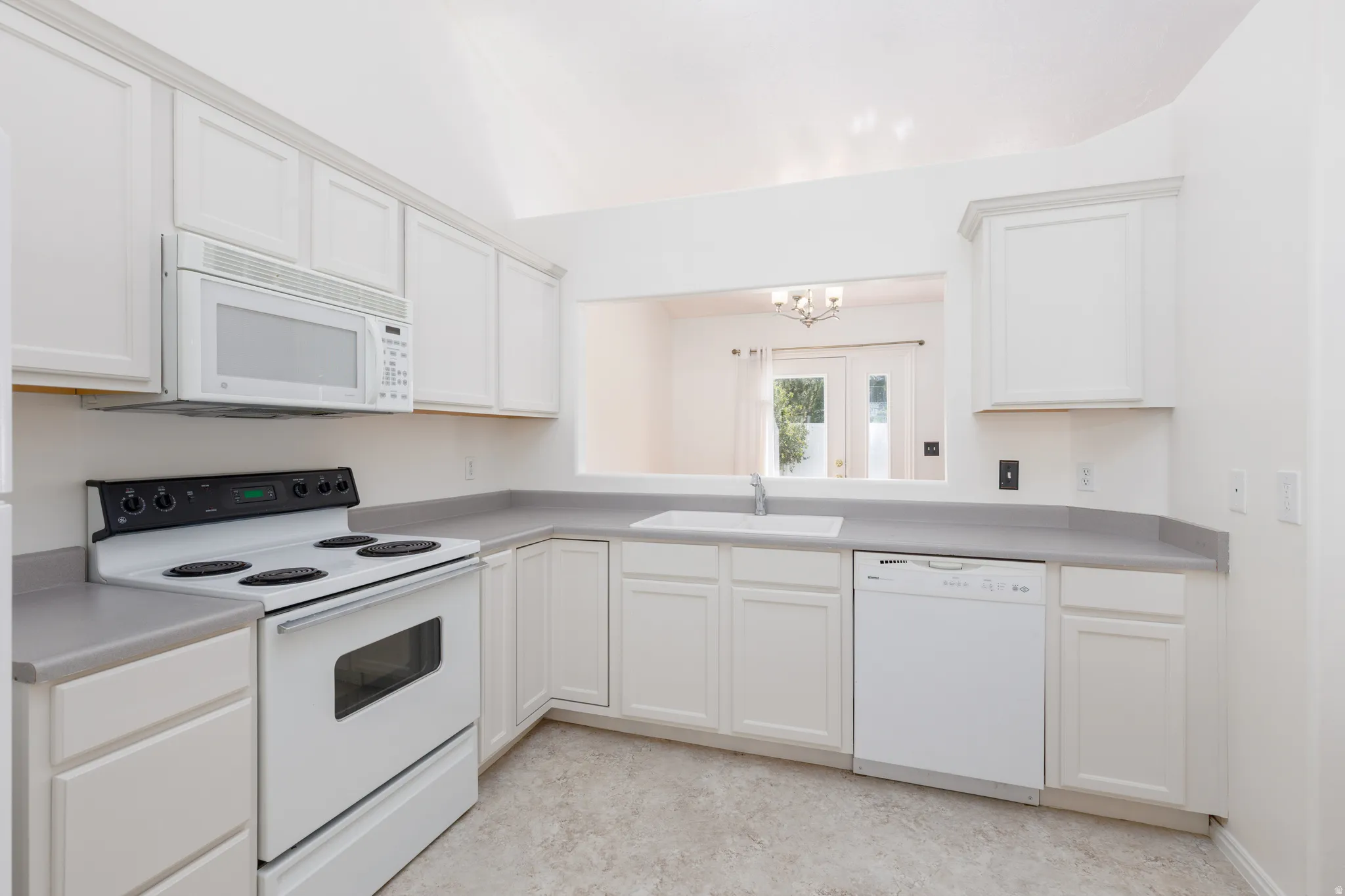 Kitchen featuring white cabinetry, light countertops, white built-in appliances, and a vaulted ceiling
