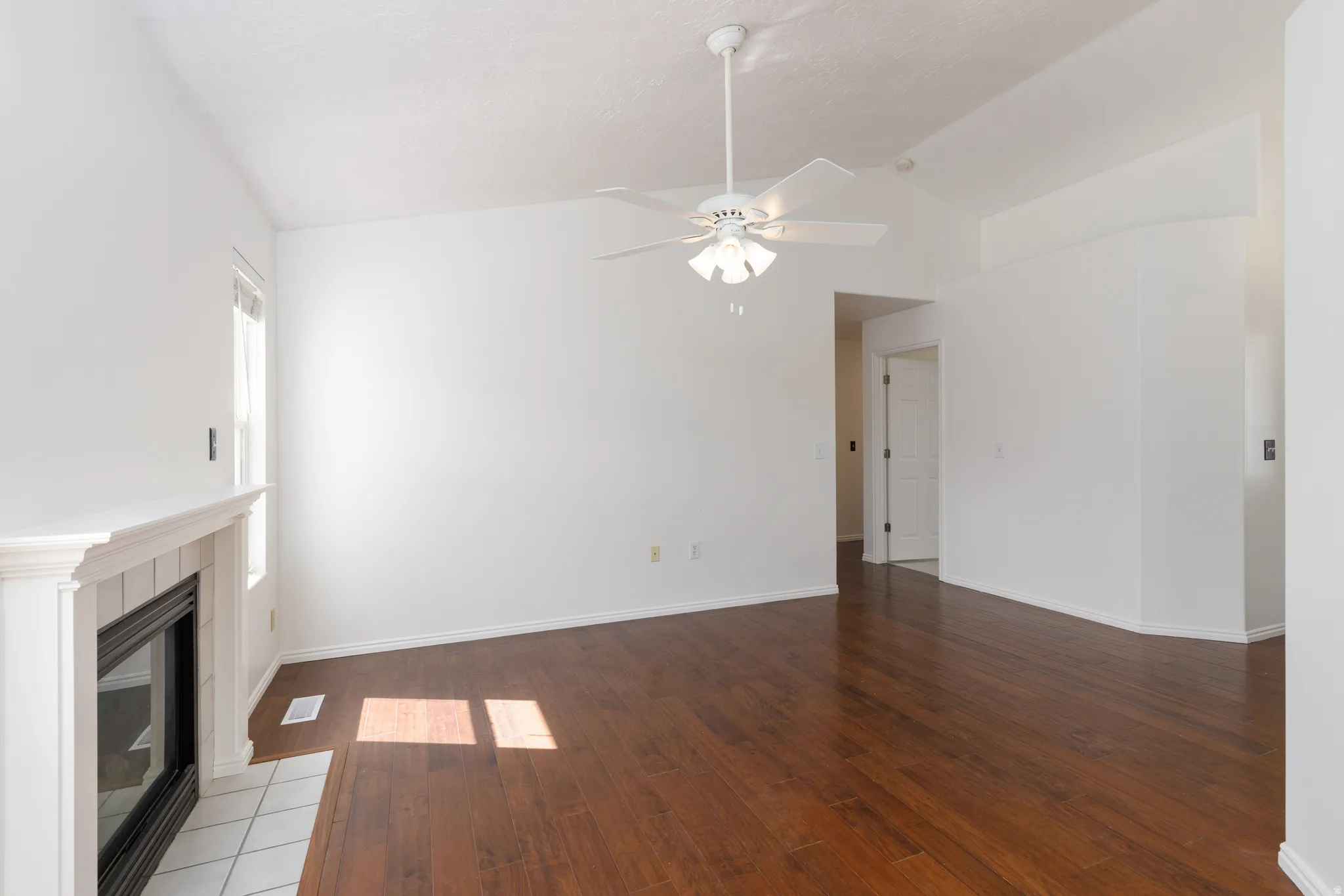 Hardwood-finish flooring with a white trim, featuring a white fireplace with a tiled hearth