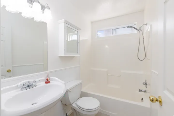 White pedestal sink with chrome faucet, wall-mounted mirror, and overhead vanity lighting