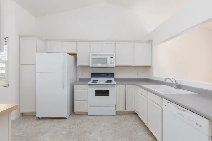 Kitchen featuring vaulted ceilings, white cabinetry, a built-in microwave, a double basin sink, and a white dishwasher