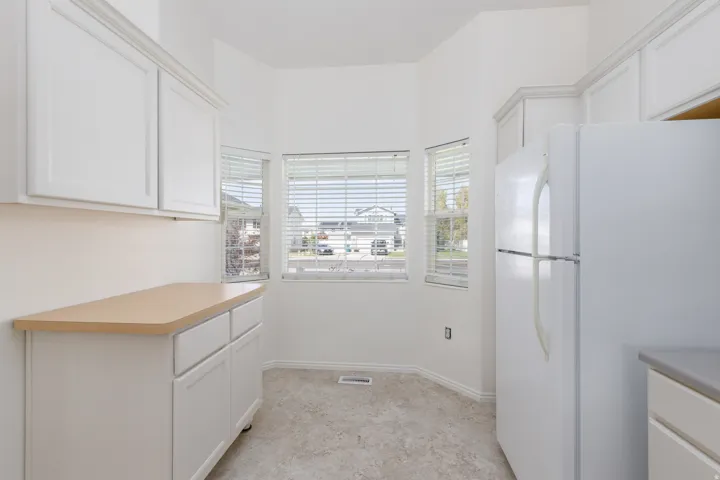 White cabinetry, light-toned countertops, and three windows with blinds