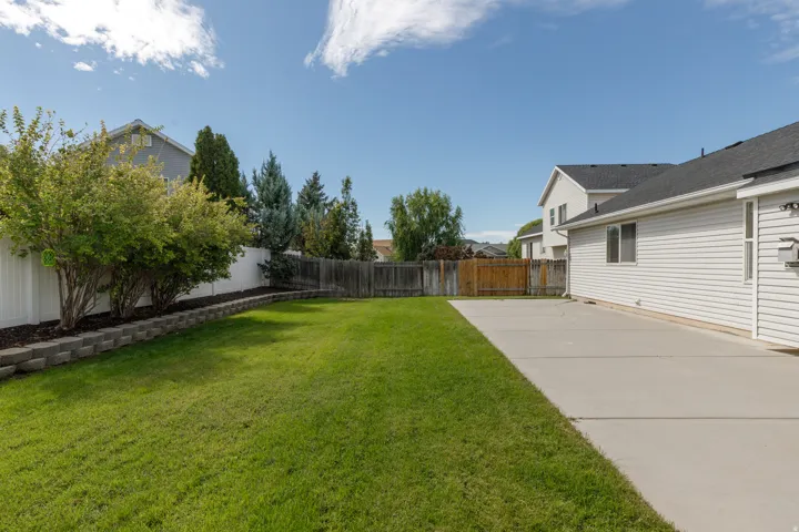 Expansive lawn area with a concrete patio, retaining wall, and mature landscaping