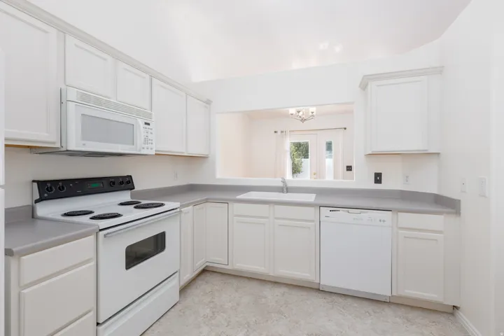 Kitchen featuring white cabinetry, light countertops, white built-in appliances, and a vaulted ceiling