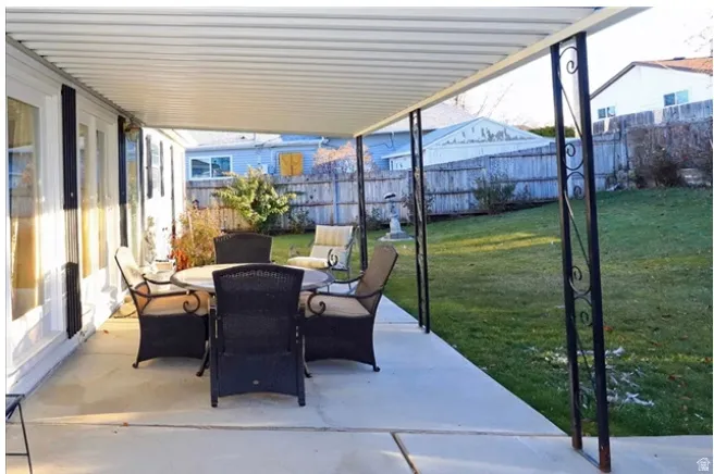 Covered patio with concrete flooring, decorative metal support columns, and access to a grass lawn