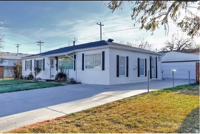 Ranch-style exterior with black shutters, a dark roof, and a concrete driveway