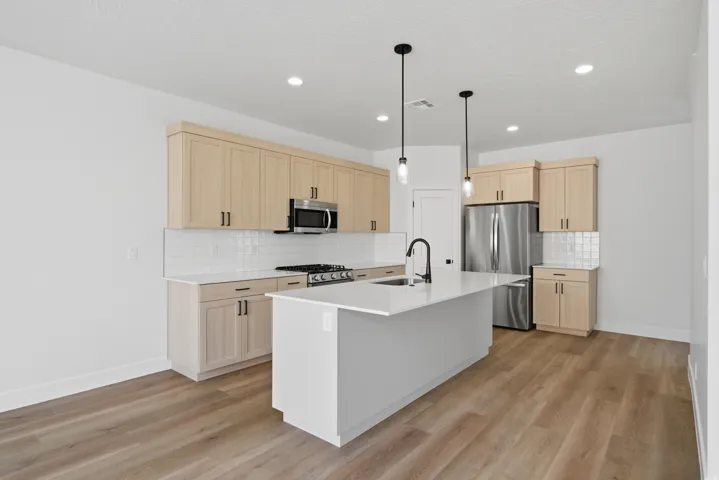 Kitchen featuring a central island, light wood-finish cabinetry, stainless steel appliances, white subway tile backsplash, and wood-finish flooring