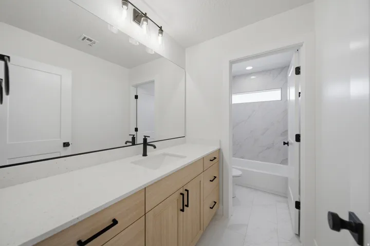 Double vanity featuring light wood-finish cabinetry, white countertops, and matte black hardware