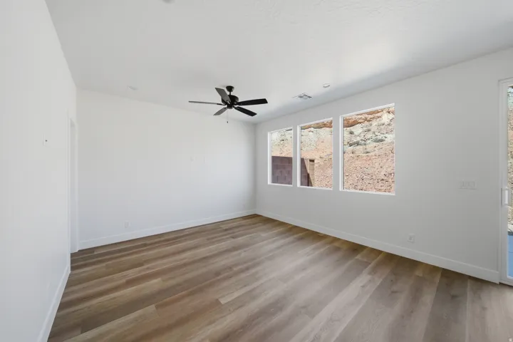 Recessed lighting, black ceiling fan, three windows with natural rock scenery, wood-finish flooring, and white walls