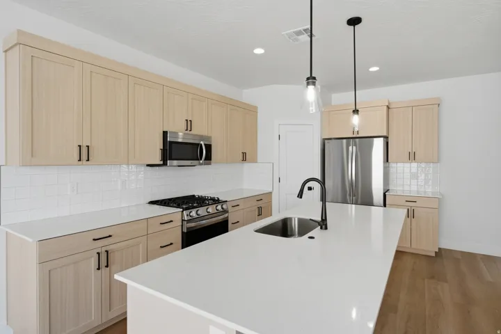 Spacious kitchen featuring light wood-finish cabinetry, stainless steel appliances, white subway tile backsplash, a large island with an undermount sink, and recessed lighting