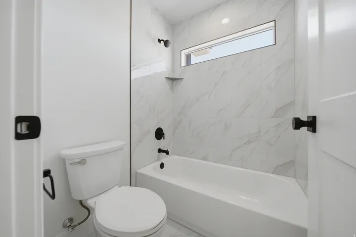 Bathtub with white subway tile surround and black fixtures, featuring a transom window and a built-in corner shelf