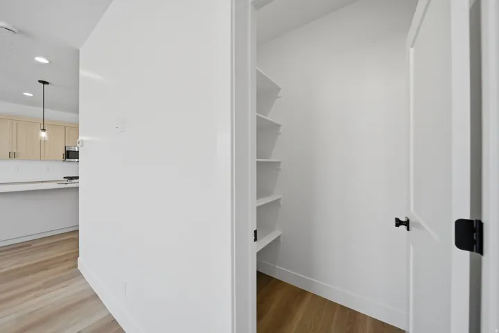 Pantry with built-in shelving, wood-finish flooring, and white interior paint