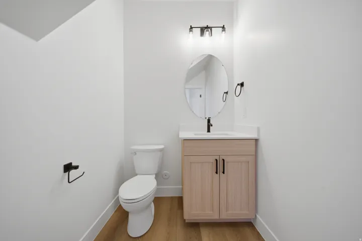 Wood-finish flooring, white walls, and a light wood vanity with a white countertop