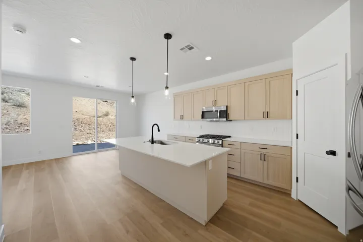 Modern kitchen featuring light wood-finish cabinetry, stainless steel appliances, a white tile backsplash, and a large island with a black faucet