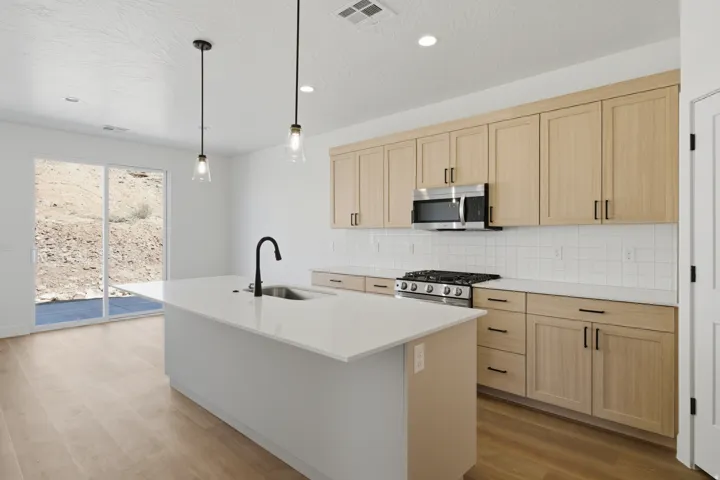 Kitchen featuring a center island with sink, light wood-finish cabinetry, stainless steel appliances, a tile backsplash, and light wood-finish flooring