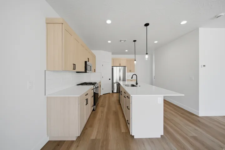 Contemporary kitchen featuring light wood-finish cabinetry, white countertops, white subway tile backsplash, and wood-finish flooring