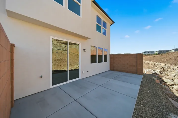 Stucco exterior with multiple windows, a sliding glass door, an exterior wall light fixture, and a concrete patio