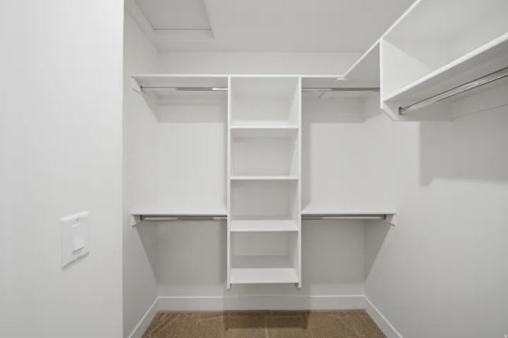 Built-in white shelving, multiple hanging rods, and carpeted flooring