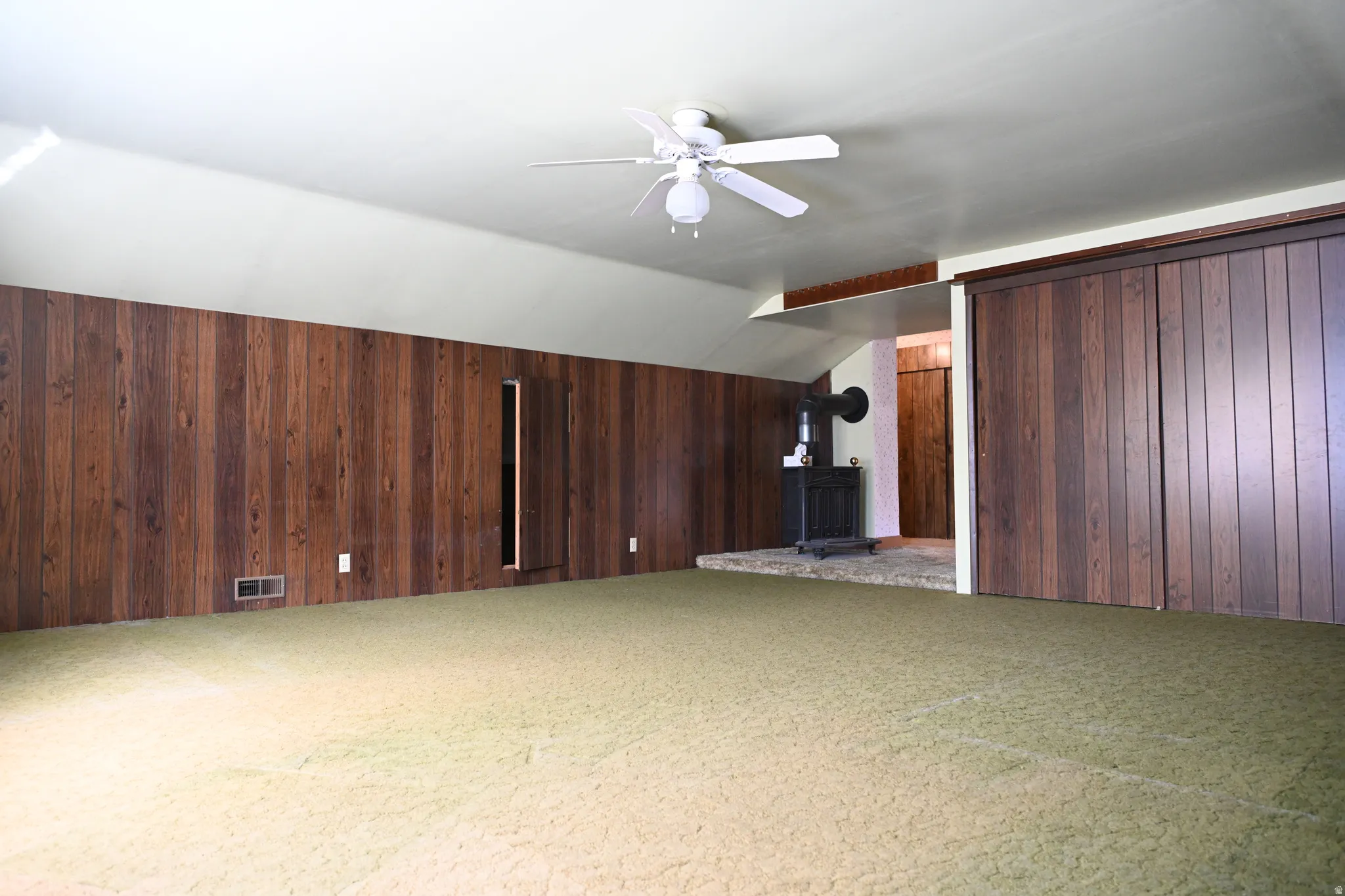 Sloped ceiling, wood paneling, ceiling fan, and built-in wood-finish sliding doors