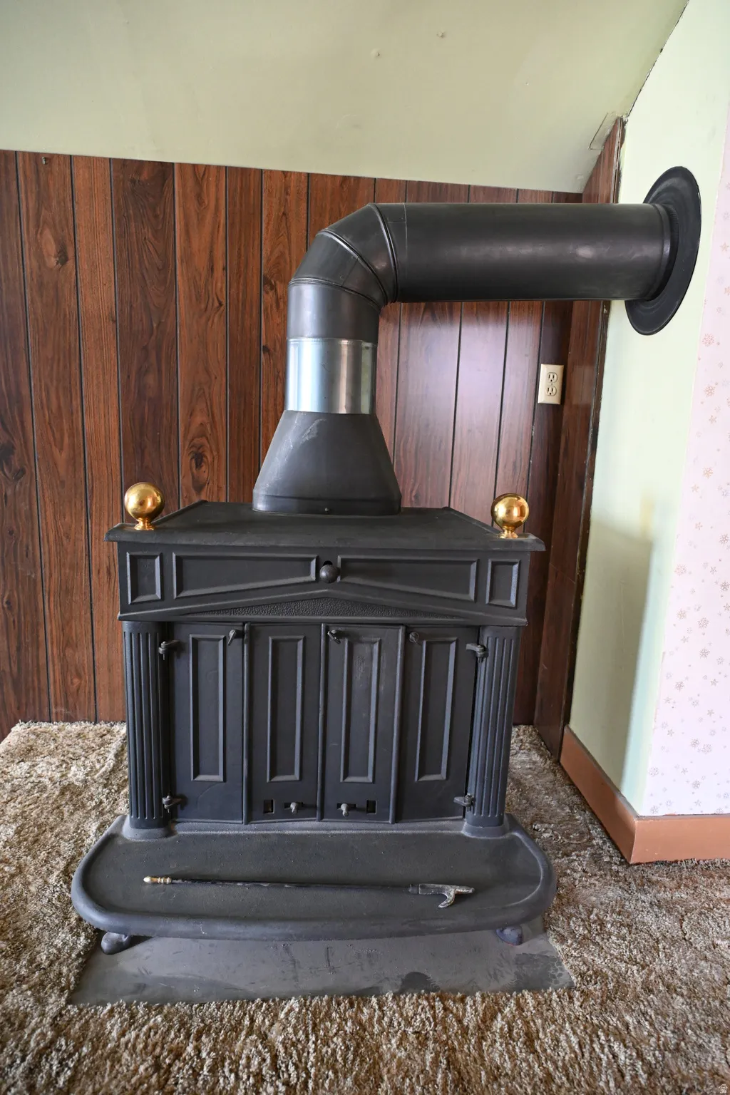 Cast iron wood-burning stove with decorative brass finials, set against wood-paneled walls