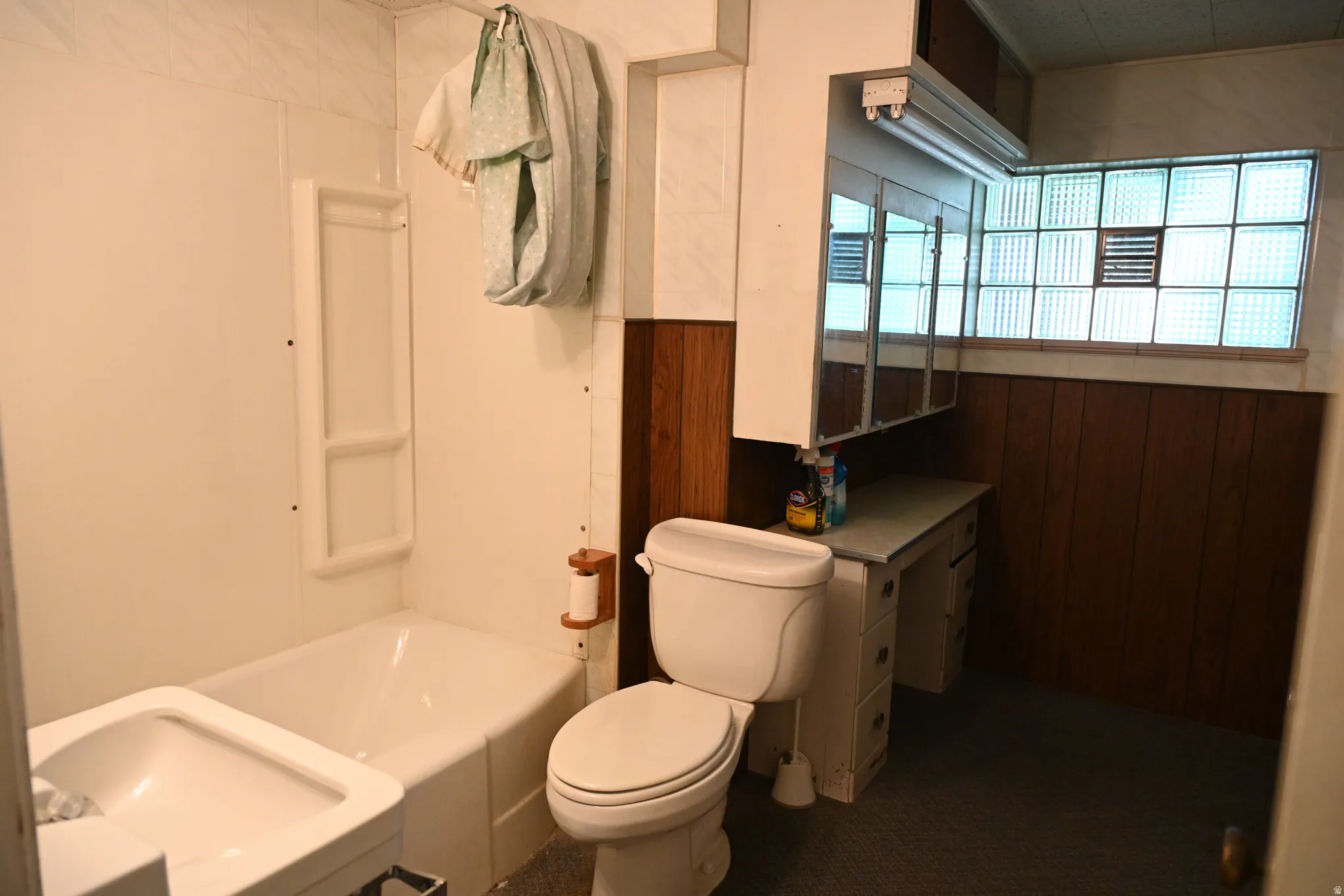 Bathtub with white surround, toilet, vanity with built-in storage, mirrored medicine cabinet, and glass block window