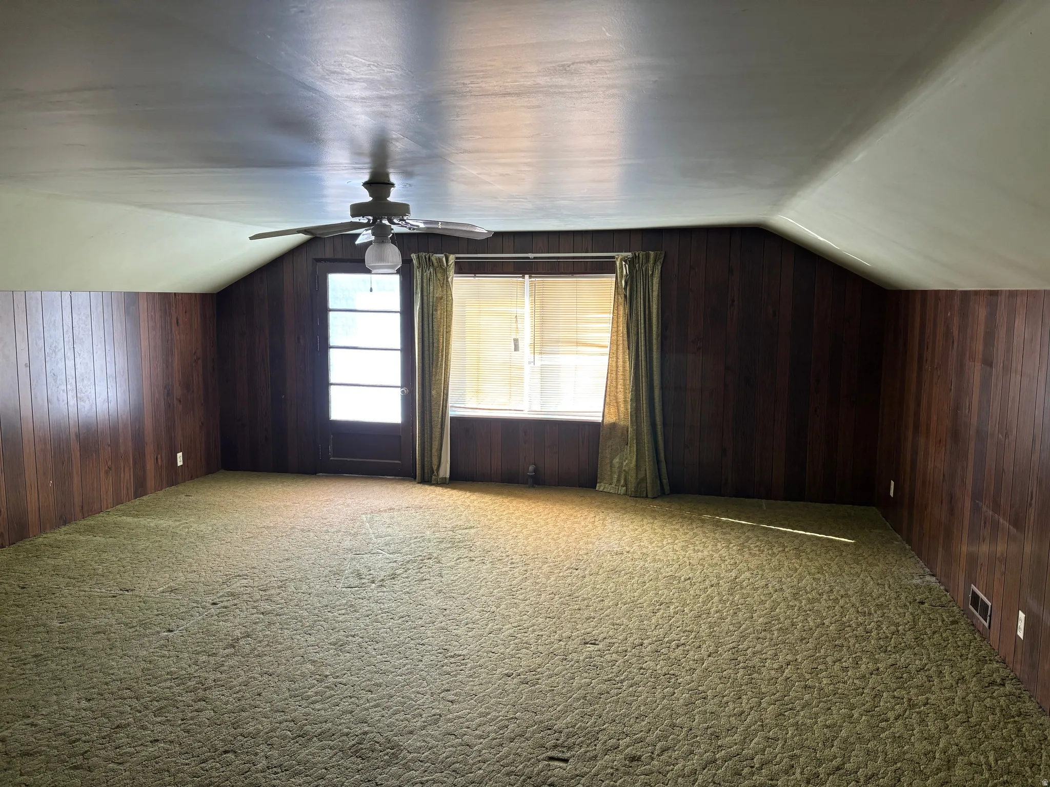 Sloped ceilings with a ceiling fan, paneled walls, and wall-to-wall carpeting