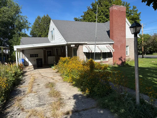 Brick and siding exterior with a peaked roofline, attached carport, and a prominent brick chimney